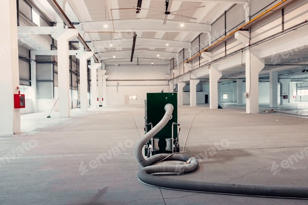 Helle leere Gewerbehalle mit Stützen und einem Industriesauger auf dem Rohboden