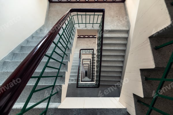 Blick von oben in ein mehrgeschossiges Treppenhaus mit Holzhandlauf