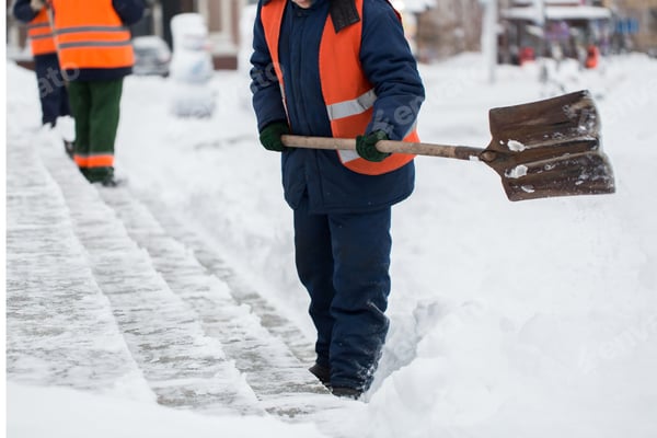 Person räumt mit einer Schneeschaufel einen Gehweg entlang einer Straße