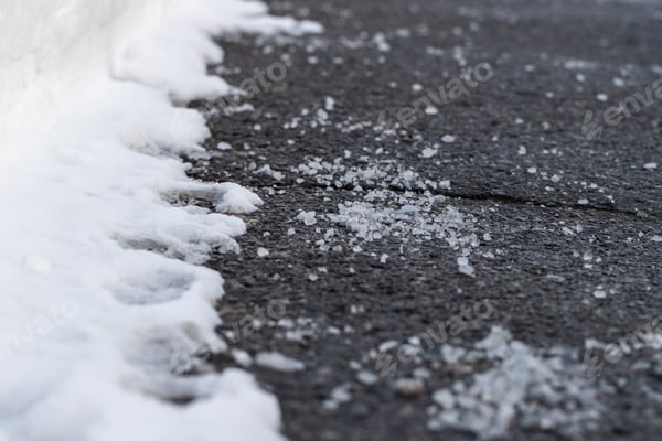 Nahaufnahme von Streugut auf feuchtem Asphalt neben einer Schneekante